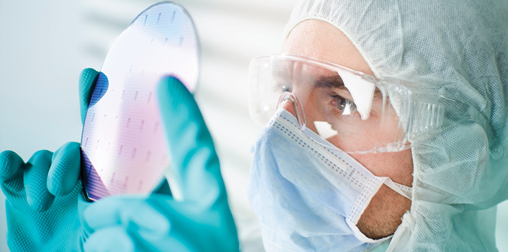 Engineer in cleanroom looking at semiconductor wafer