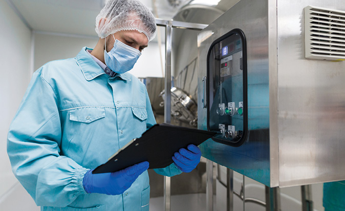 Man with clipboard and protective suit in front of a machine